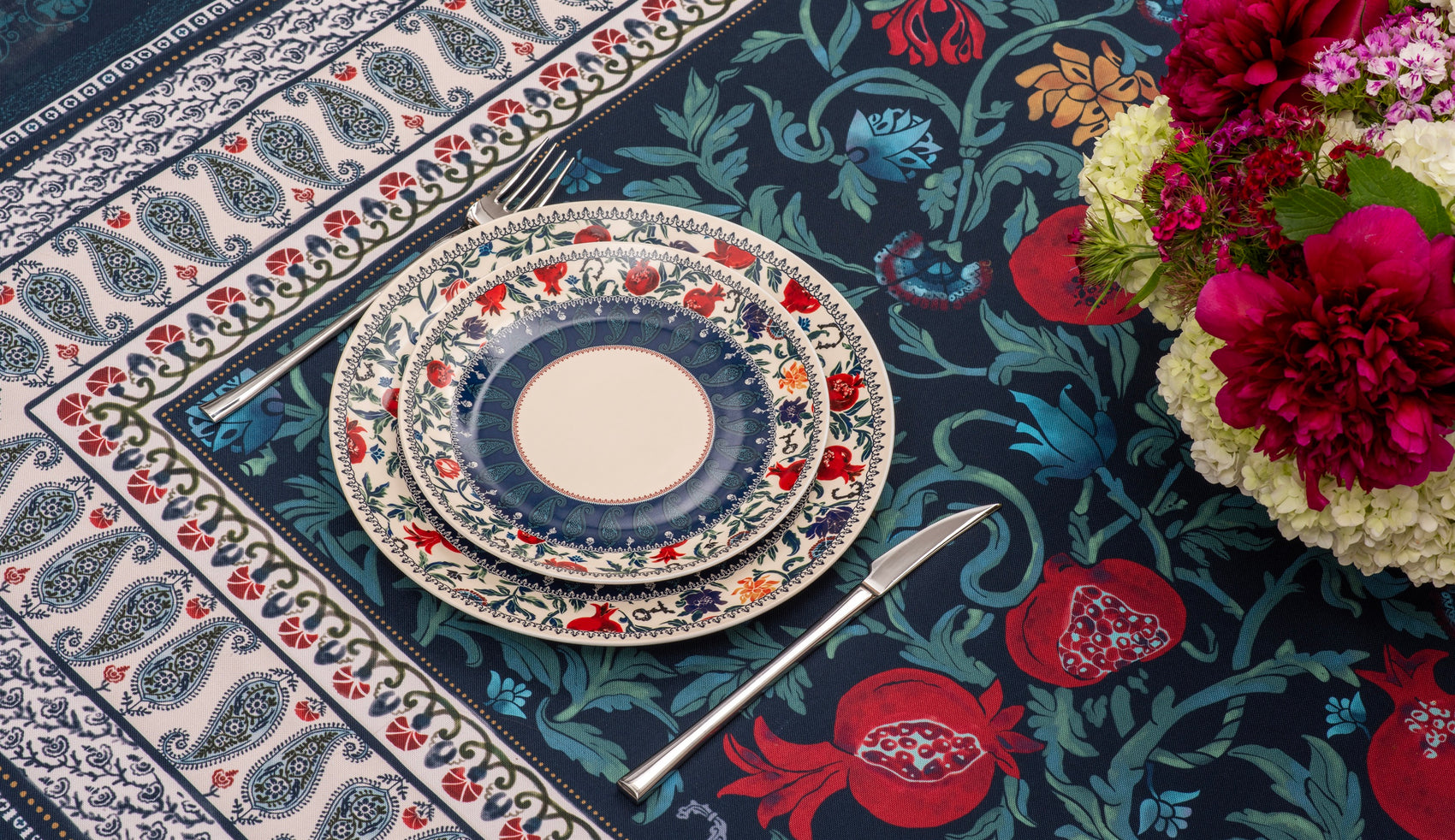 Corner view of the BlueTabla Georgian Alphabet & Pomegranate blue tablecloth with a place setting and floral centrepiece.