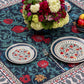 BlueTabla Georgian Alphabet & Pomegranate blue tablecloth styled with stacked patterned plates, apples and a peony bouquet.