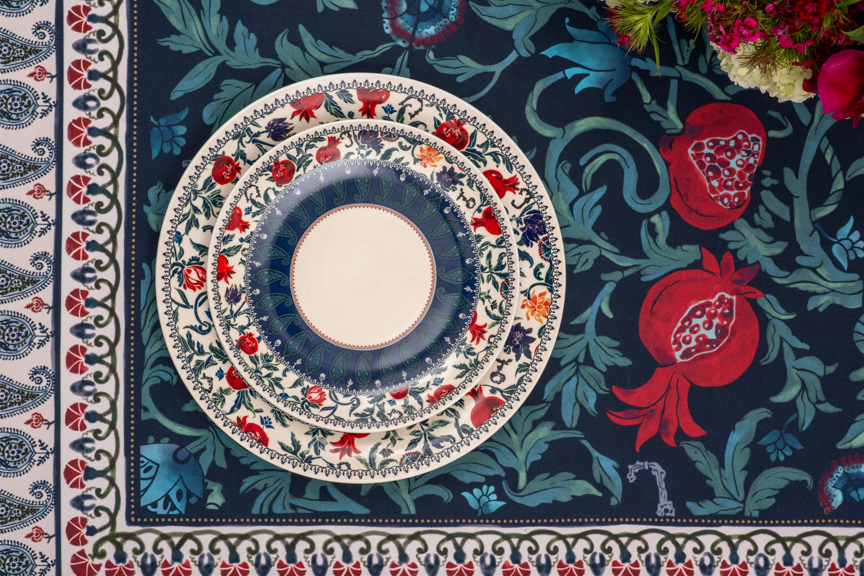Stacked patterned plates on the BlueTabla blue tablecloth, showing the pomegranate and Georgian alphabet motif in detail.
