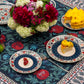 BlueTabla blue tablecloth set for tea with patterned plates, a peony and hydrangea bouquet, fresh fruit and lemon desserts.