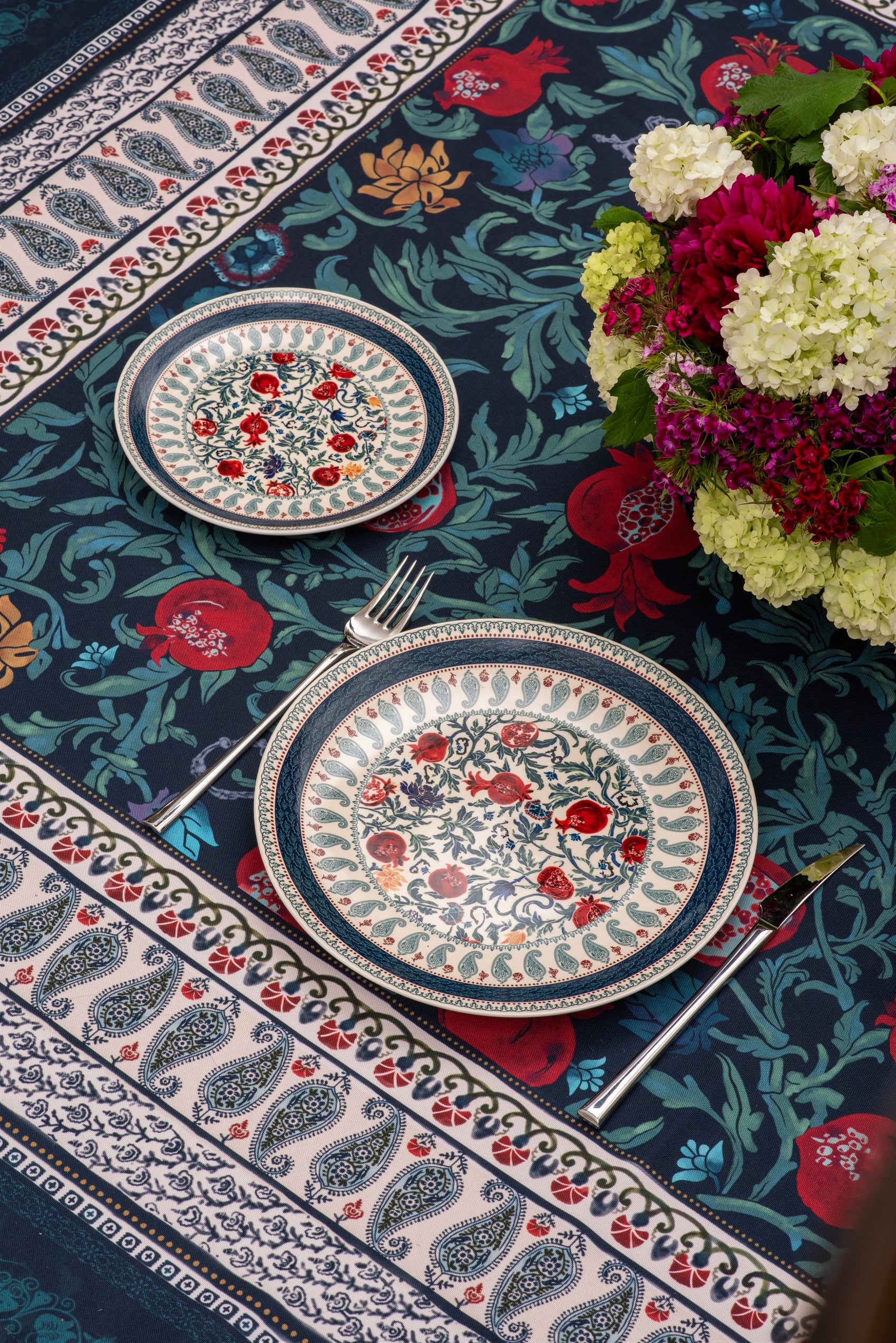 Two patterned place settings on the BlueTabla blue pomegranate tablecloth, with paisley border and hydrangea bouquet.